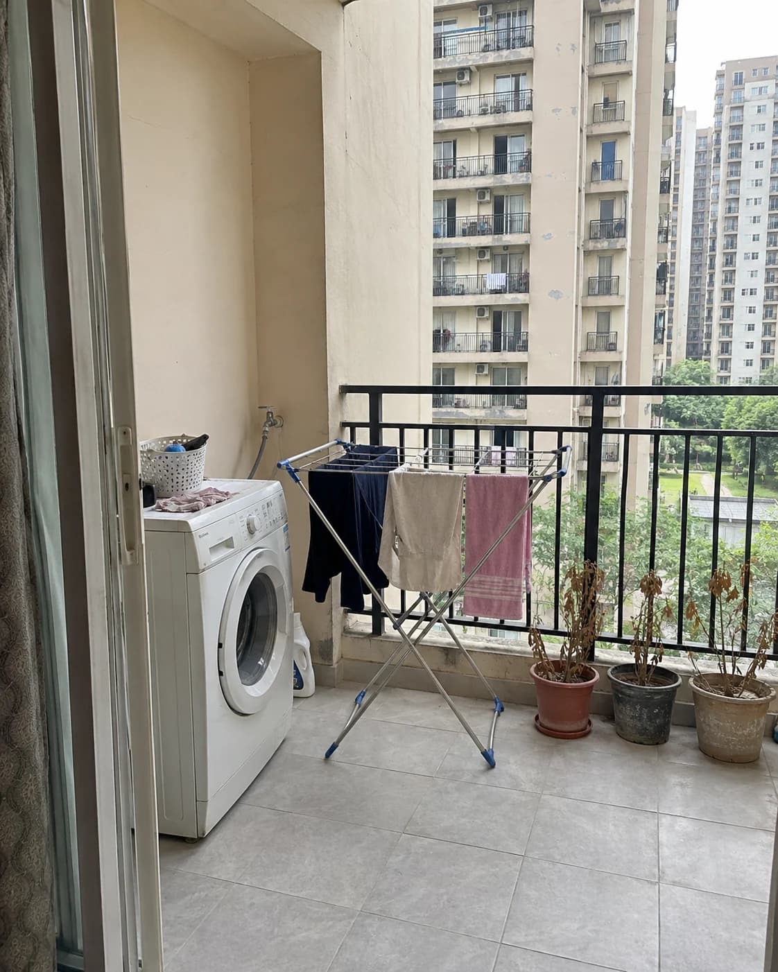 A bare apartment balcony with a washing machine and a drying stand